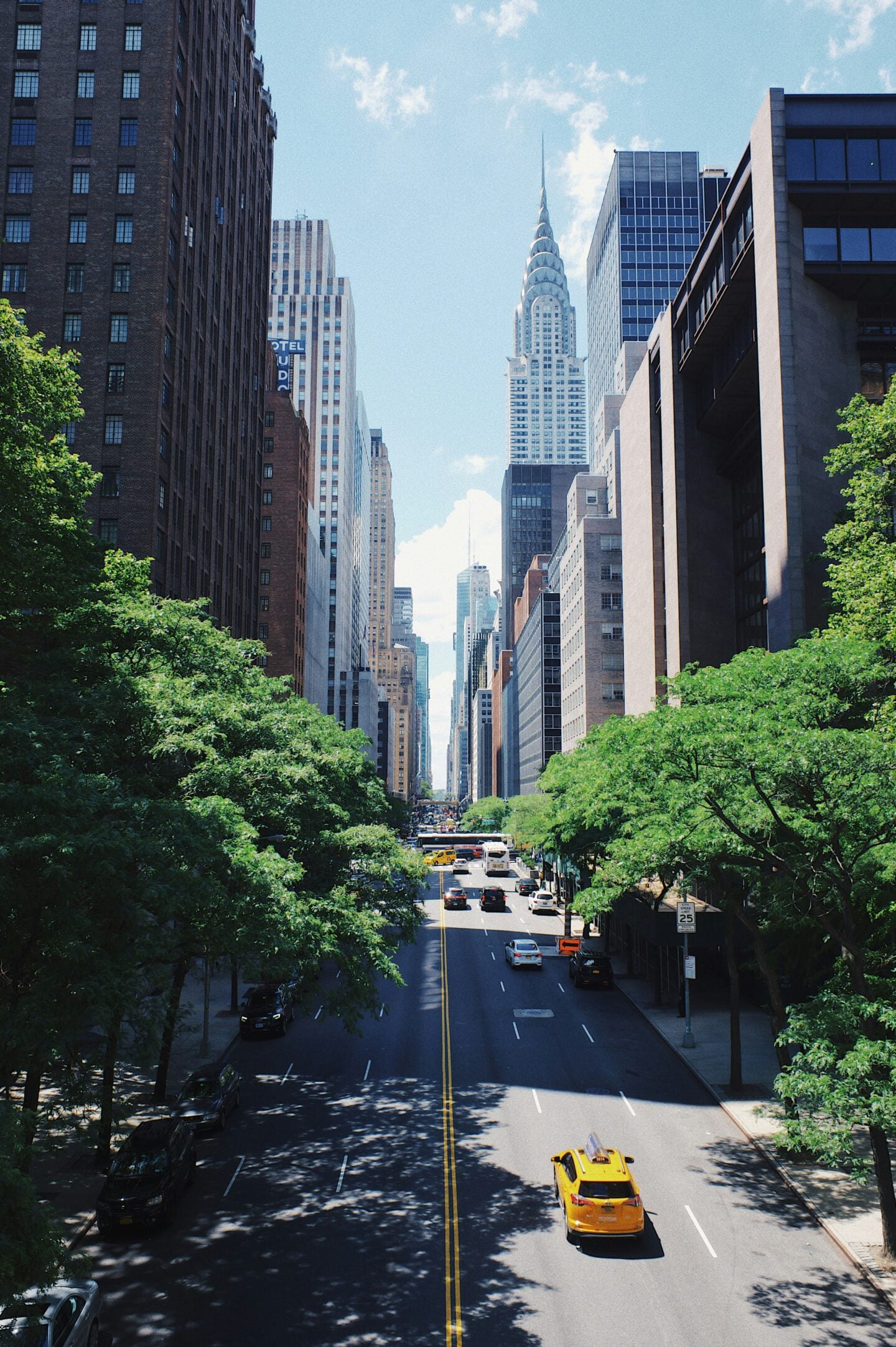 Tree-lined Manhattan street with yellow taxis and tall buildings framing the Chrysler Building beneath a blue sky.
